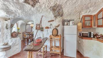 Una cocina rústica con paredes de piedra, una mesa de madera y un refrigerador blanco.
