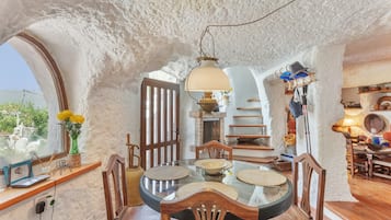 Un comedor con una mesa de vidrio, sillas de madera, una lámpara colgante y vistas a través de un arco.
