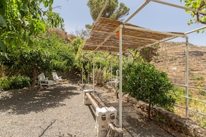 A covered outdoor seating area with chairs, a pergola, and a view of a hilly landscape.