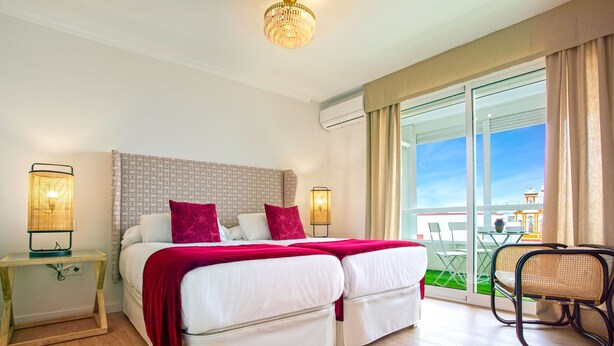 A double bed with white bedding and red accents, a bedside table with a lamp, and a view of an outdoor area with a table and chairs. - Stunning Apartment With City Views. San Pablo (Seville)