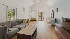 A spacious living room with a large sofa, a coffee table, and a TV. There is a wooden floor and a large window with a view of the outside. - House w/ garden & terrace – 6 adults/2 kids (La Baule-Escoublac)