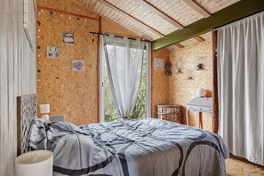 A bedroom with a bed, a bedside table, a chair, a window with curtains, and a wall with birdcages.