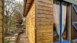 Eine Holzhütte mit einer Terrasse, großen Fenstern und Blick auf Bäume.