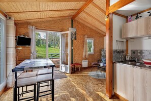 A wooden interior with a dining table, kitchen area, and large windows.