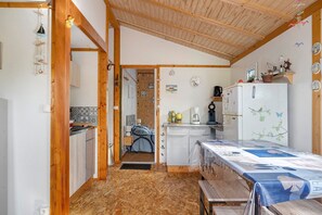 A compact kitchen with wooden beams, a refrigerator, a sink, and a dining table with a tablecloth.
