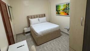 Ein kleines, ordentlich eingerichtetes Schlafzimmer mit Bett, Kleiderschrank, Nachttisch und einem Bild an der Wand.