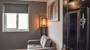 A room with a dark wall, a window with blinds, a cushioned bench, a framed artwork, and a dark wooden door with a glass panel. - The Signature Residence (Newsome)