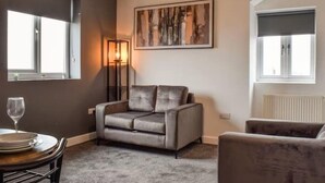 A living room with a grey sofa, a dining table with chairs, a floor lamp, and a painting on the wall. - The Signature Residence (Newsome)