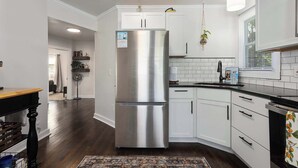 A modern kitchen with white cabinets, a stainless steel refrigerator, a black countertop, and a patterned rug. - Modern Style_Sleeps 8_Walkable Area_Fenced Yard (Lee's Summit)