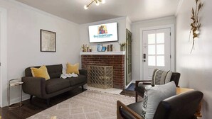 A living room with a fireplace, a television mounted on the wall, and a door to the right. - Modern Style_Sleeps 8_Walkable Area_Fenced Yard (Lee's Summit)