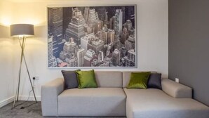 A modern living room with a grey sectional sofa, a floor lamp, and a cityscape painting on the wall.