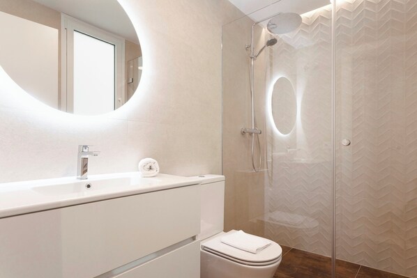A modern bathroom with a glass shower enclosure, a round mirror, and a white sink.