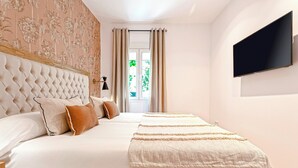 Een slaapkamer met een gestapeld hoofdbord, een groot bed met meerdere kussens, een nachtkastje met een lamp en een aan de muur bevestigde televisie.