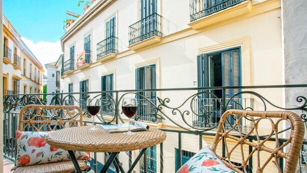 Een balkon met rieten meubels, een tafel en twee wijnglazen.