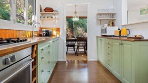 A kitchen with green cabinets, a wooden countertop, and a dining area with chairs and a table. - The Hidden Cottage (Tootgarook)