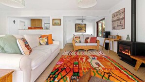 A living room with a white sofa, a colorful rug, a fireplace, and a large window. - The Hidden Cottage (Tootgarook)