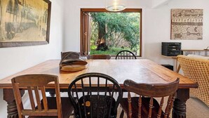 A dining area with a wooden table, black chairs, and a large window offering a view of greenery. - The Hidden Cottage (Tootgarook)