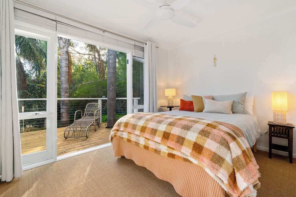 Une chambre avec un grand lit, une table de chevet, une chaise et une vue sur une terrasse et des arbres.