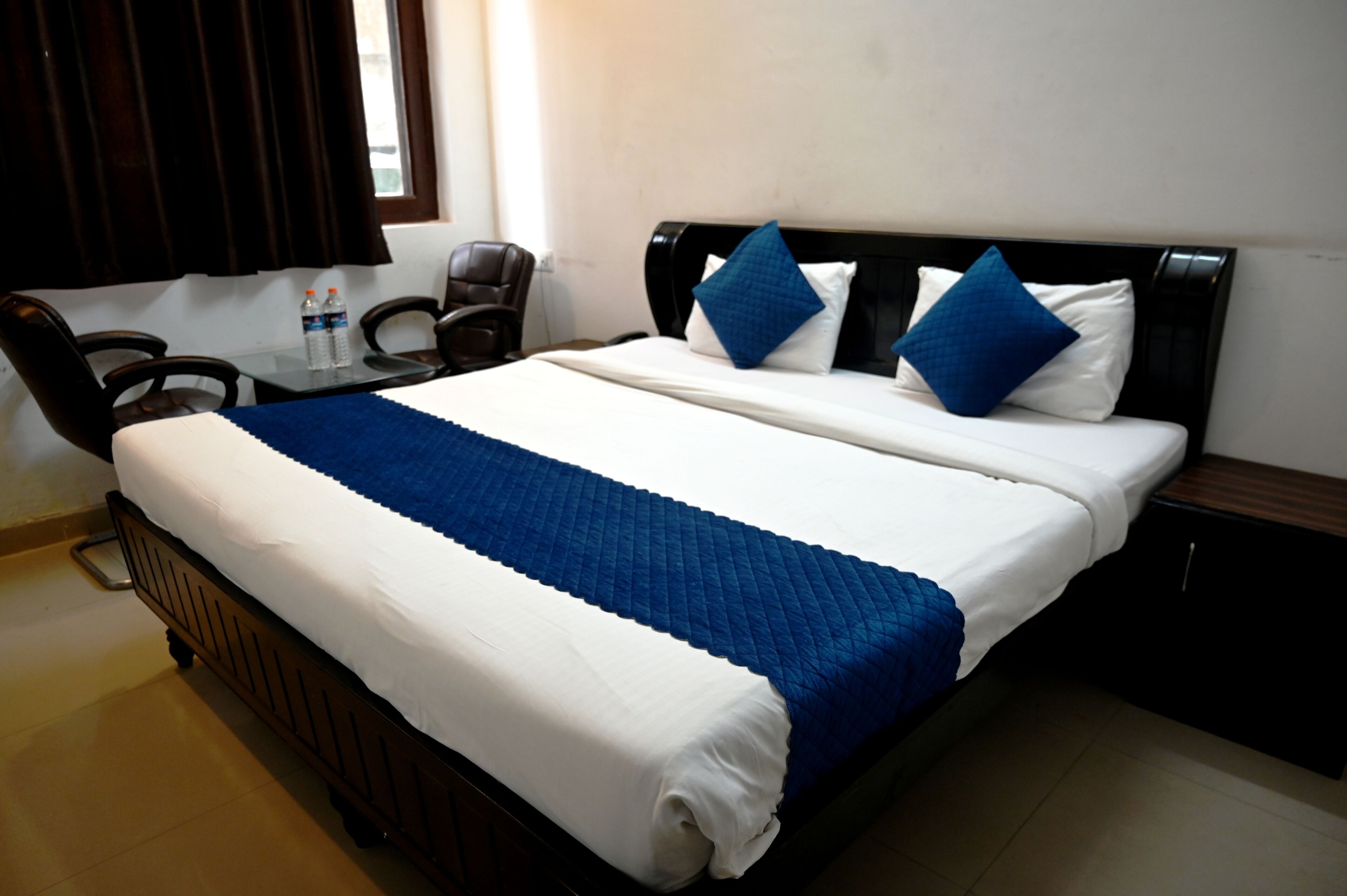 Ein ordentlich bezogenes Bett mit einer blauen und weißen Tagesdecke, zwei blauen Kissen und einem hölzernen Kopfteil.