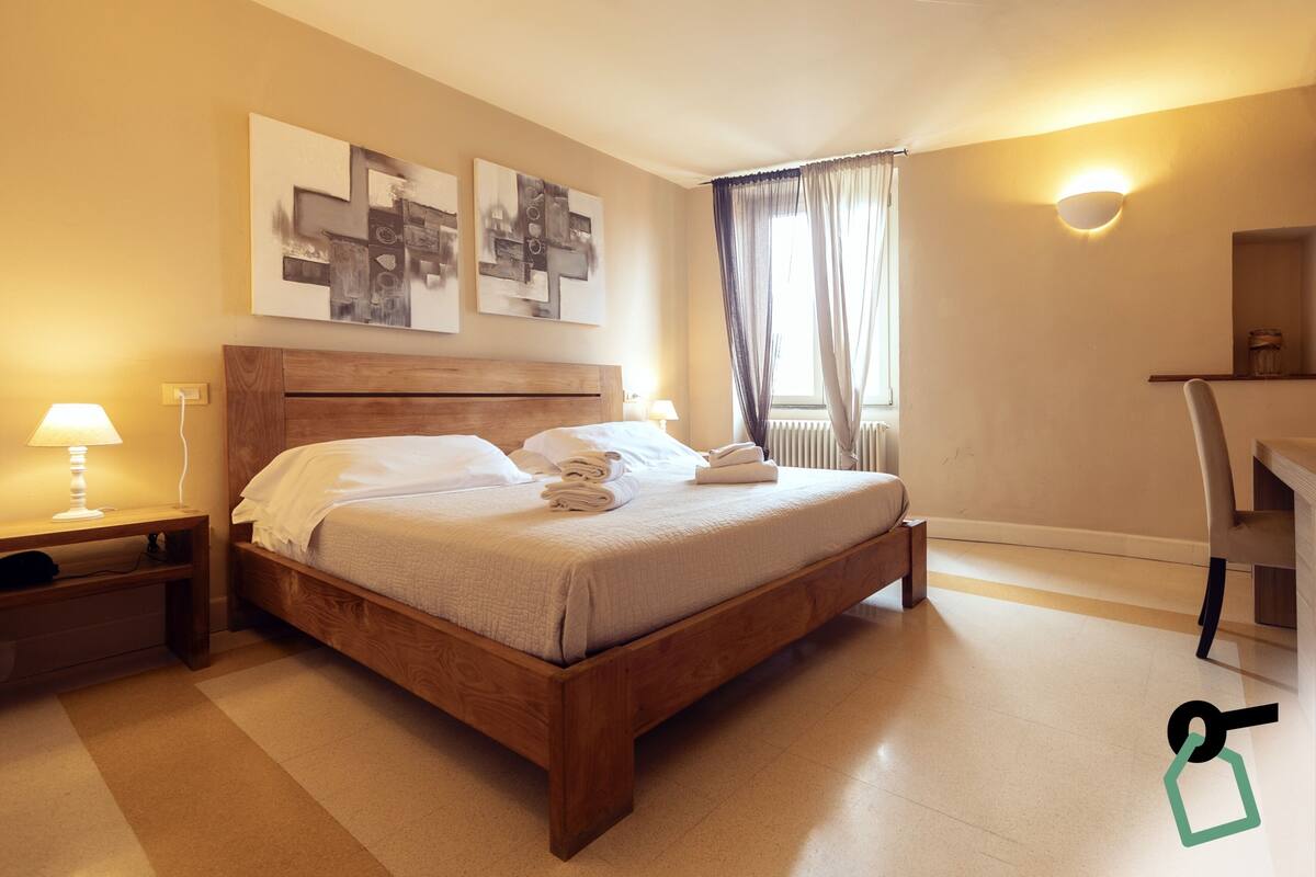 Un lit bien fait, avec du linge de lit blanc, une tête de lit en bois et deux lampes de chevet.