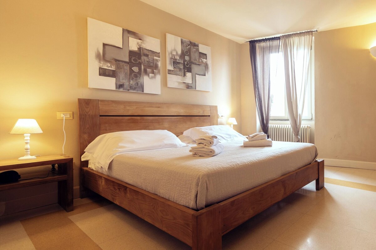 Een opgemaakt bed met witte lakens, een houten hoofdbord en twee bedlampjes.