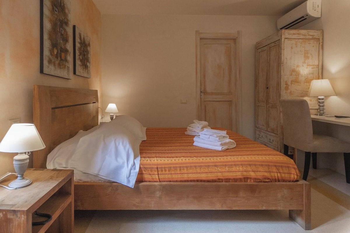 Une chambre d’hôtel avec un lit en bois, deux lampes de chevet, un bureau avec une chaise et un appareil de climatisation.