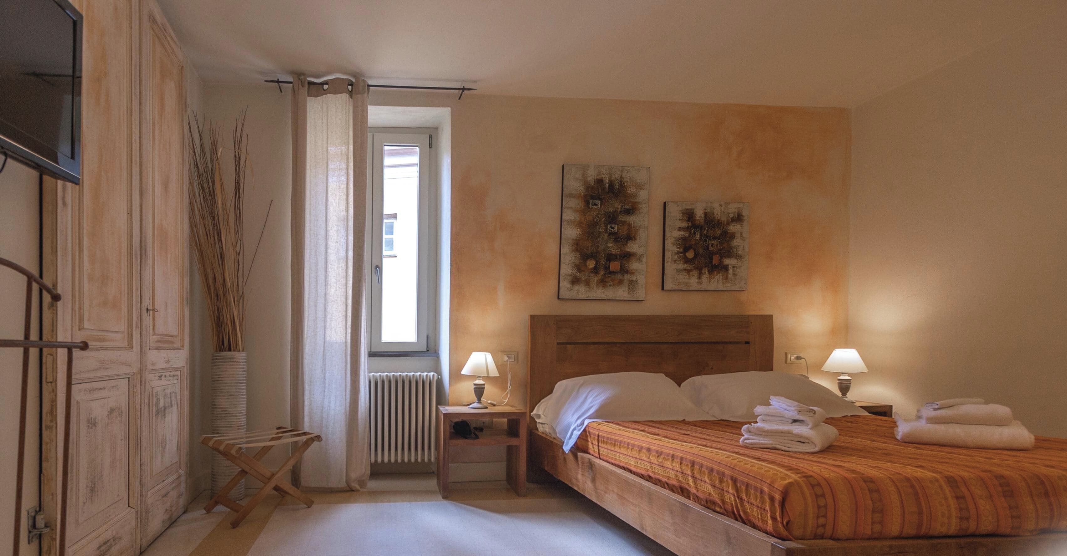 Une chambre à coucher avec un lit, deux lampes de chevet, un radiateur et une fenêtre avec des rideaux.