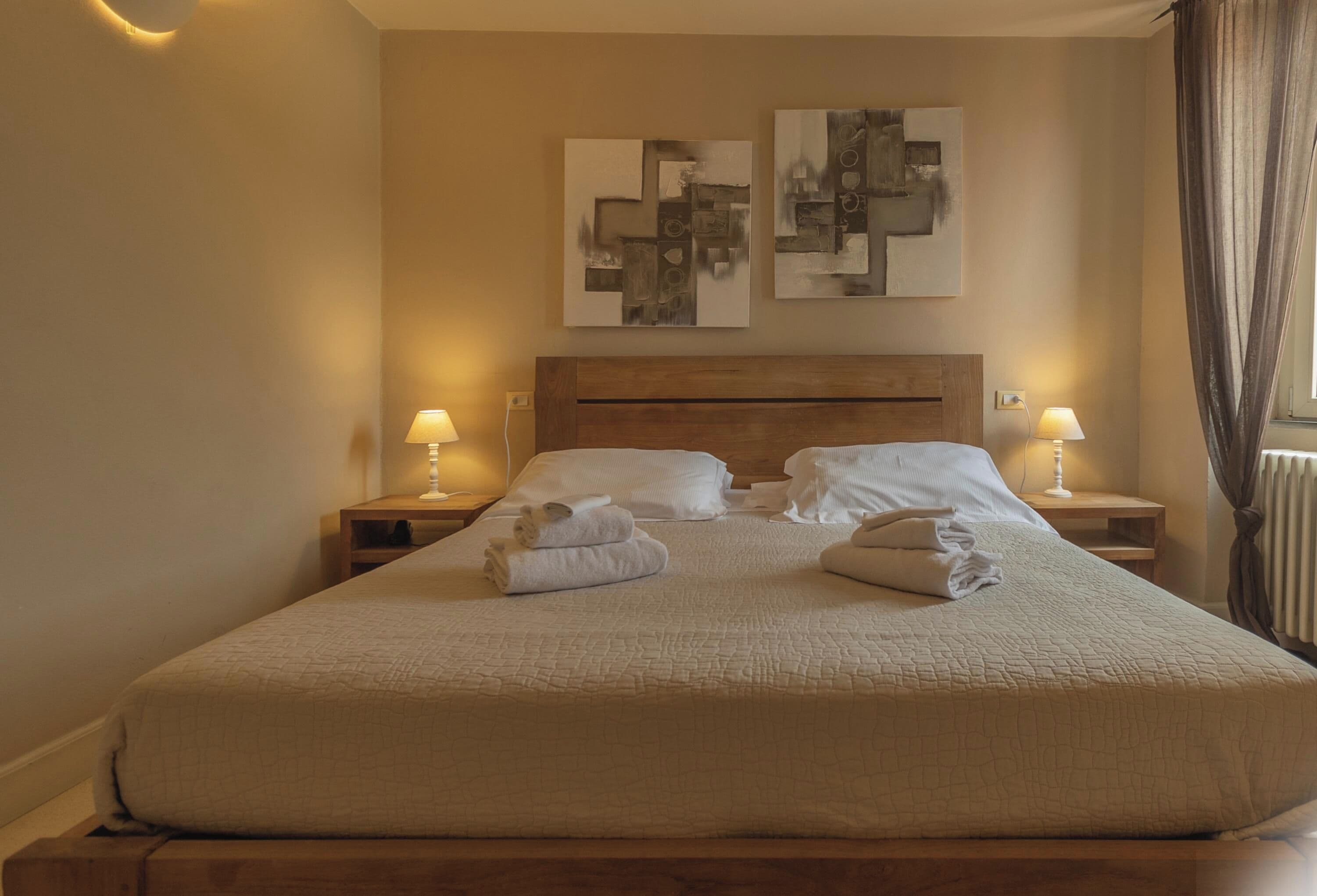 A neatly made bed with a wooden headboard, two bedside lamps, and artwork on the wall.