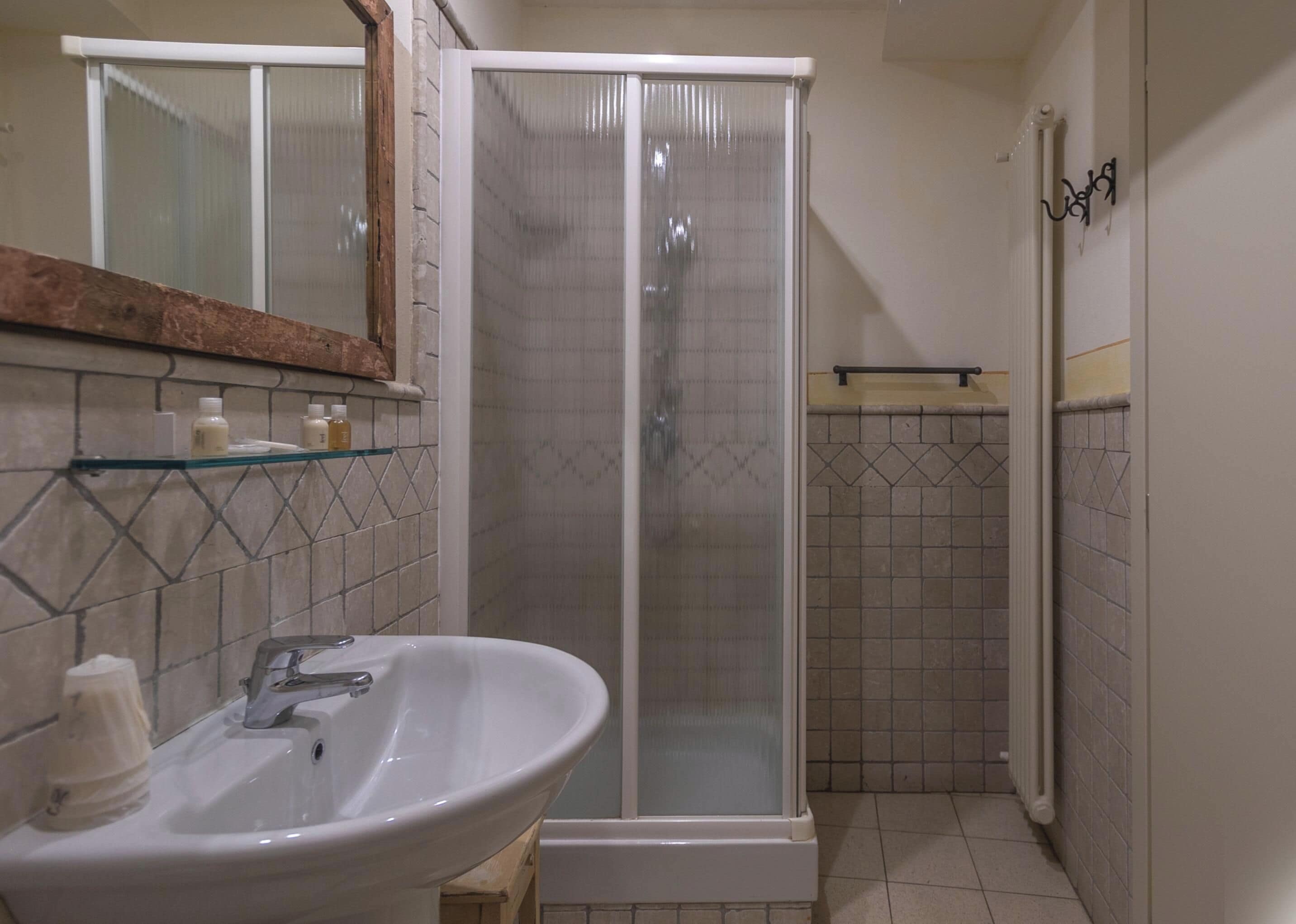 Un baño con lavamanos blanco, cabina de ducha de vidrio y zona de ducha con azulejos.