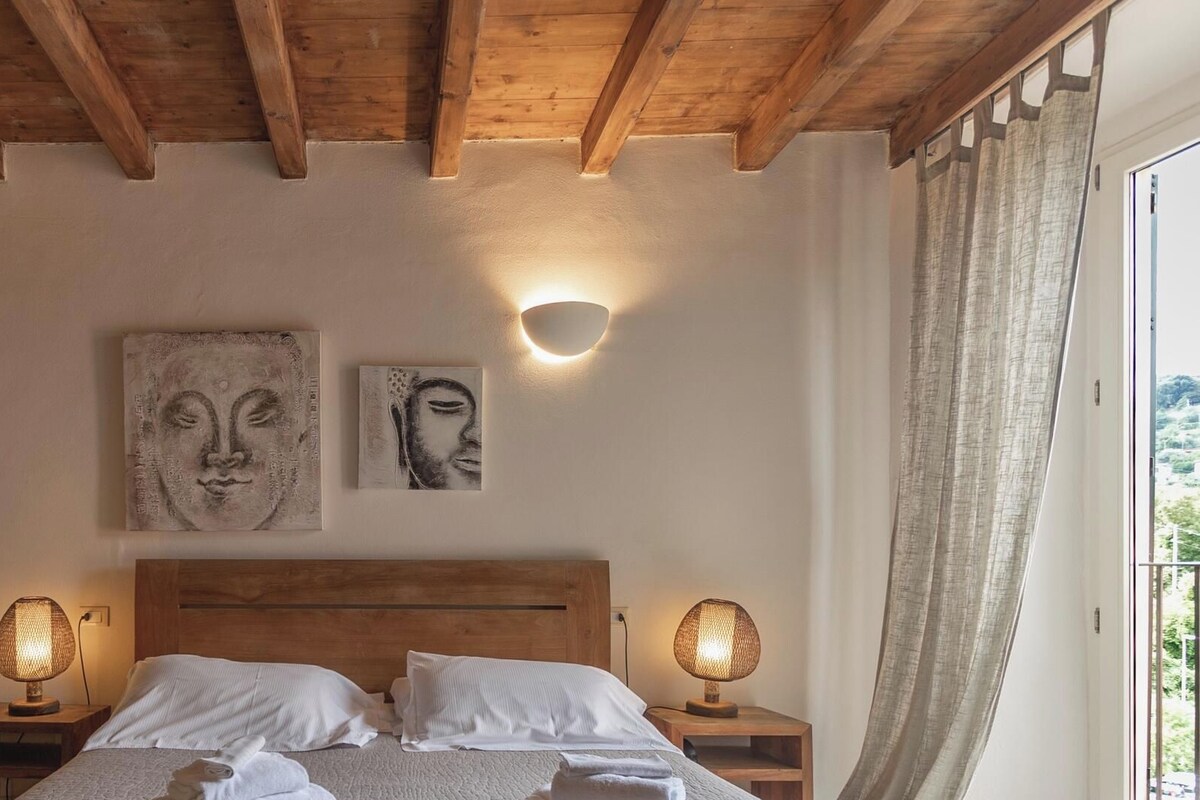 A bedroom with a wooden ceiling, two bedside lamps, a bed with white bedding, and two wall-mounted artworks.