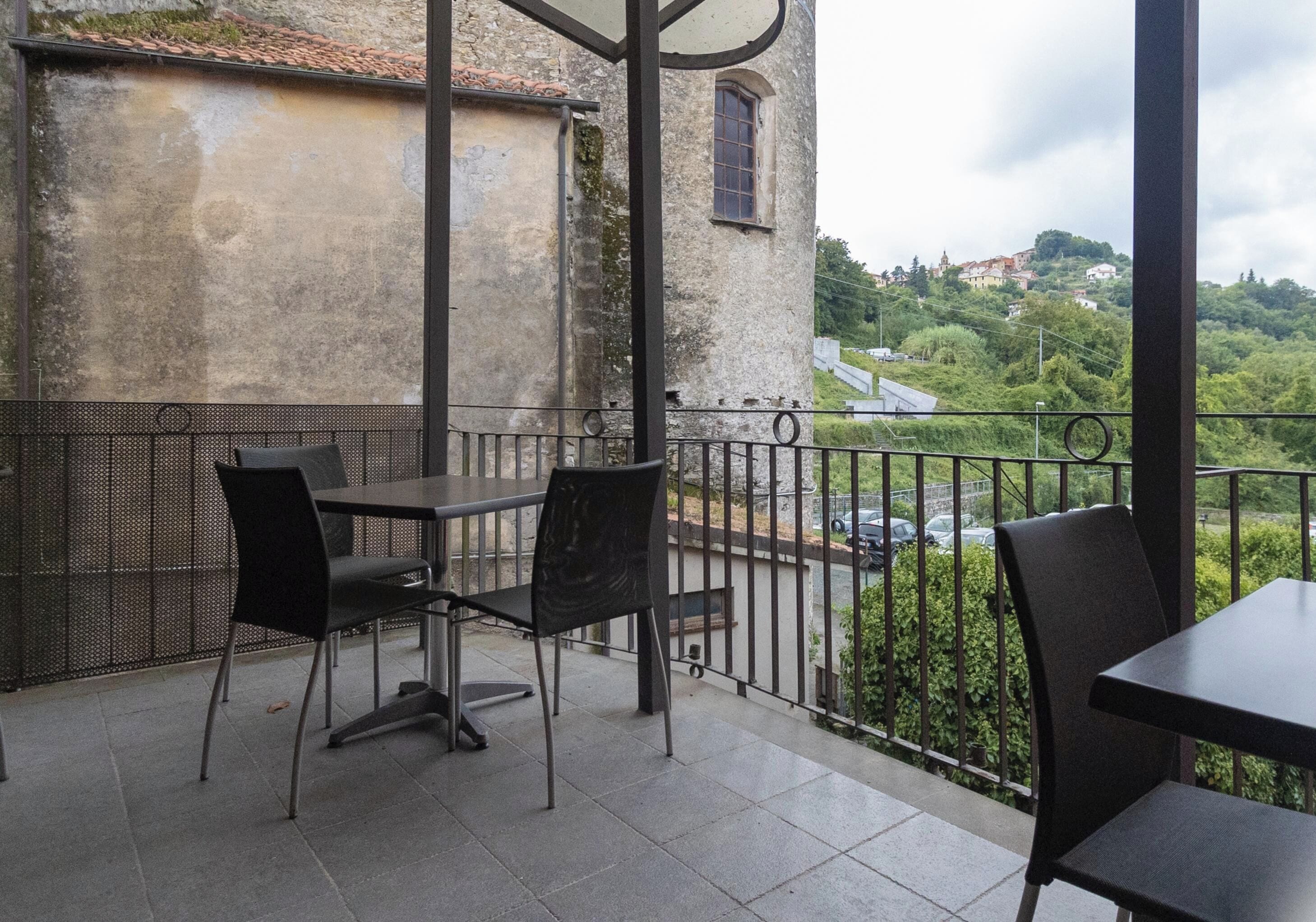 Un balcón con dos mesas y sillas, que da a un edificio de fachada de piedra y vistas de un paisaje verde con colinas.
