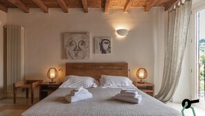 Un dormitorio con techo de madera, una cama grande con ropa de cama blanca, dos lámparas de pared y una obra de arte en la pared.