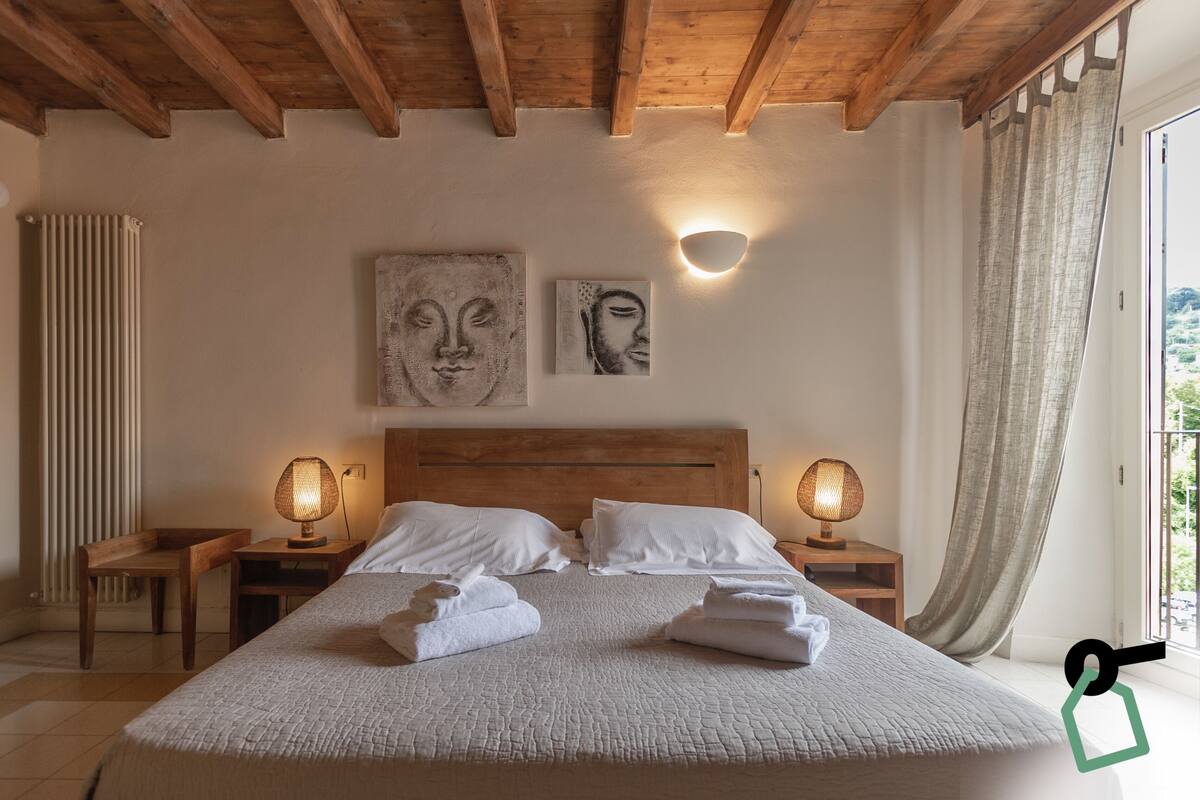 Une chambre avec un plafond en bois, un grand lit avec une literie blanche, deux lampes fixées au mur et des œuvres d’art accrochées au mur.