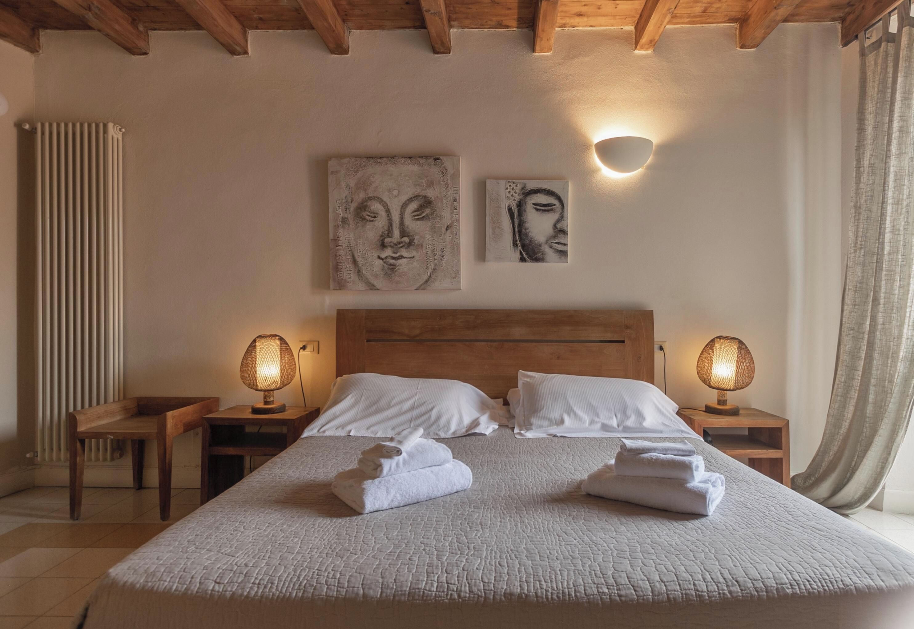 Un dormitorio con techo de madera, una cama grande con ropa de cama blanca, dos lámparas de pared y una obra de arte en la pared.