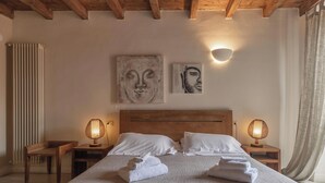 A bedroom with a wooden headboard, two bedside lamps, a bed with white linens, and two wall-mounted artworks.