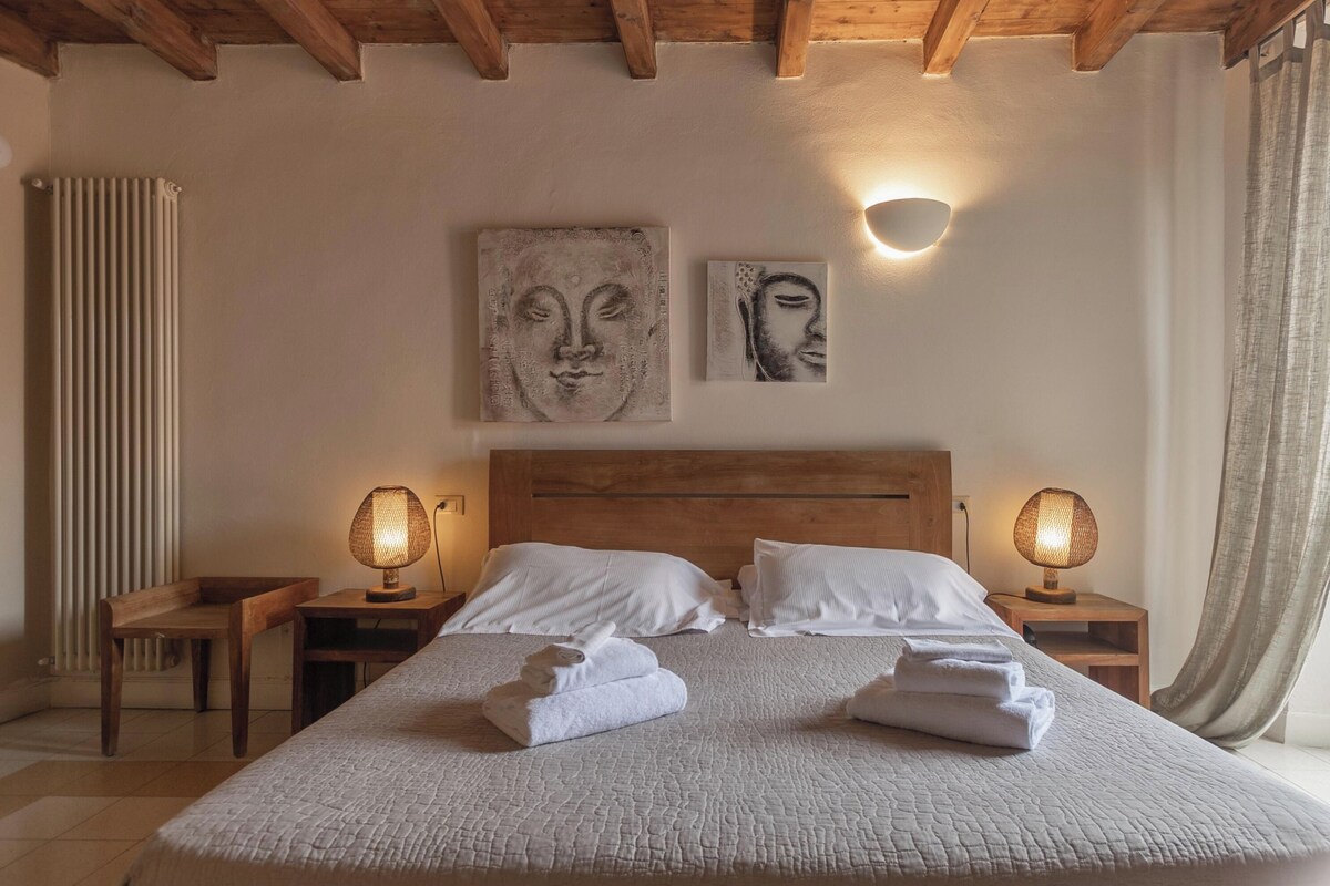 Een slaapkamer met een houten plafond, een groot bed met wit beddengoed, twee wandlampen en kunst aan de muur.