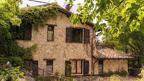 A stone building with multiple windows and a tiled roof, surrounded by greenery and rocks. - Flight Country Resort (Castel dell'Aquila)