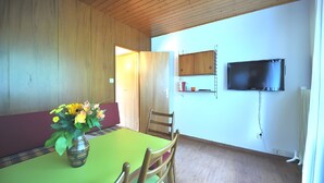 Ein Essbereich mit Holzbalkendecke, einem grünen Tisch und einem Blumenstrauß.