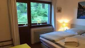 Une chambre d’hôtel avec un lit, une table avec un carnet et un stylo, une fenêtre donnant sur un paysage verdoyant et une lampe.