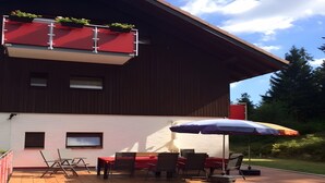 Un bâtiment à deux étages doté d’un balcon, d’un espace extérieur aménagé avec une table et des chaises, et d’une terrasse en bois.