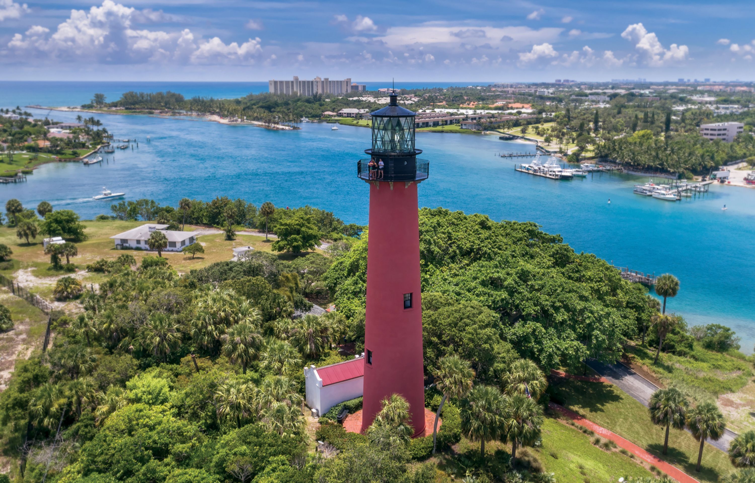 Un phare rouge, entouré d’une végétation luxuriante, et un port de plaisance avec des bateaux.