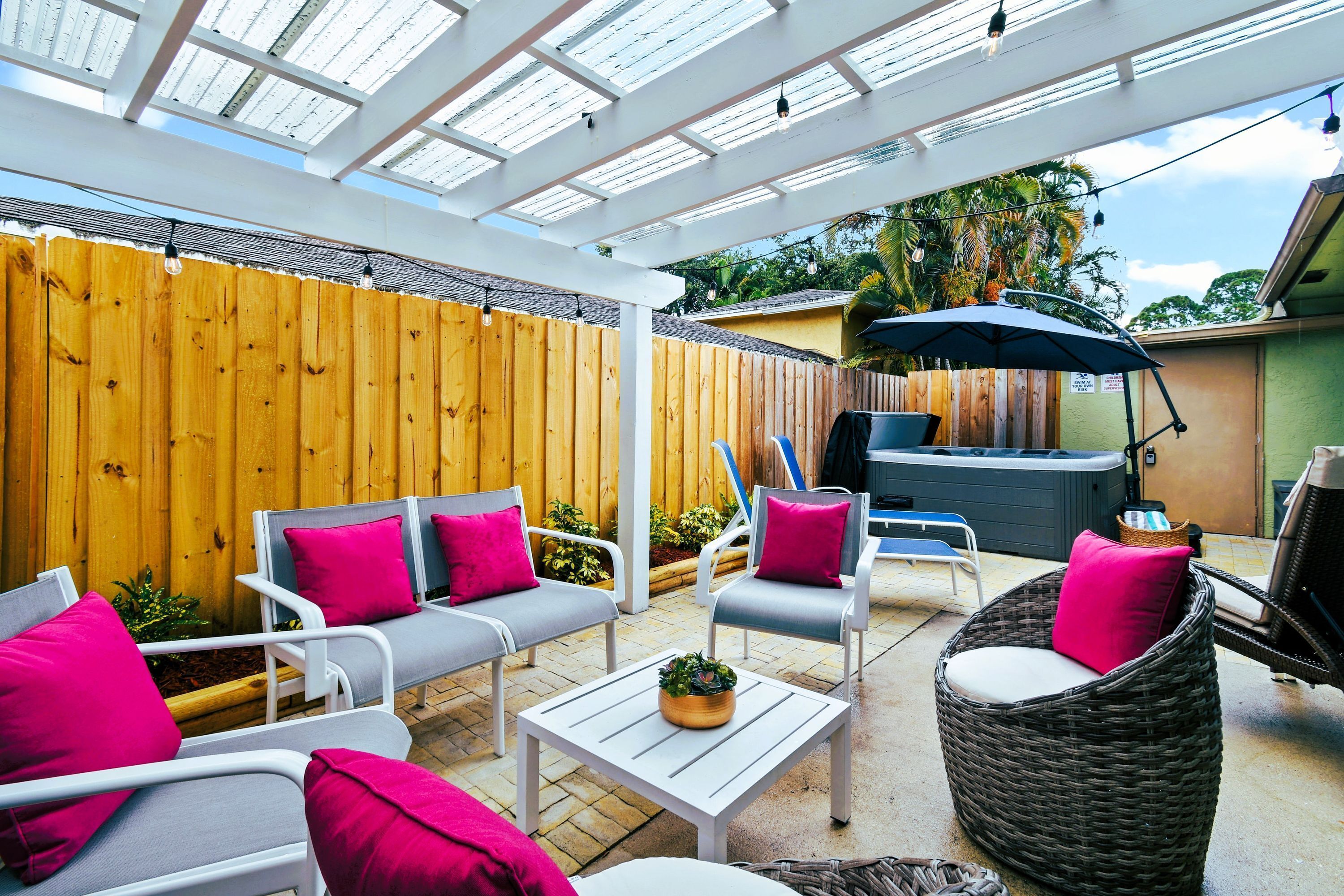 Un patio techado con mobiliario exterior, una parrilla y una valla de madera.