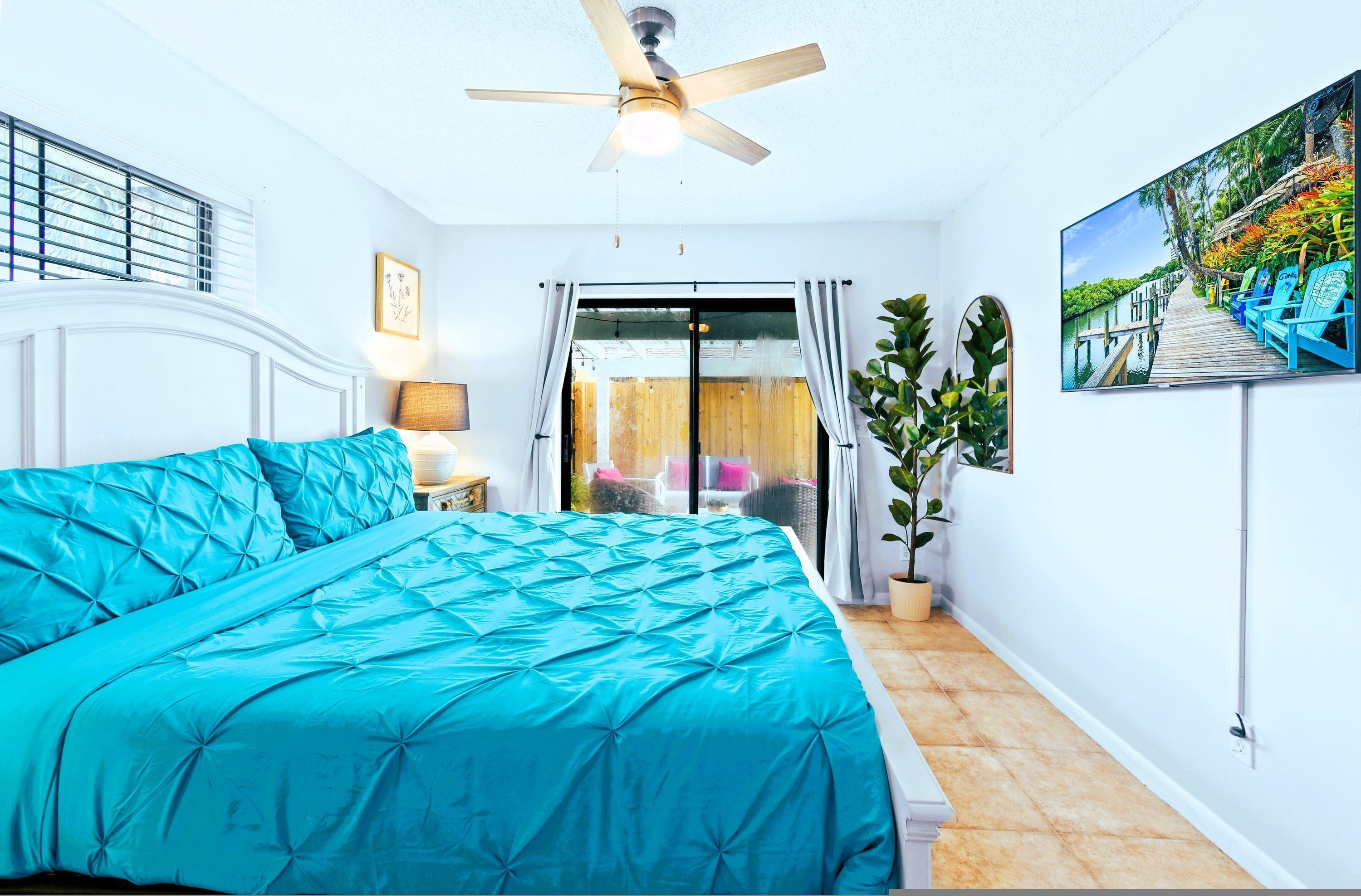 Un dormitorio con cama, ventilador de techo, televisor y vistas al exterior.