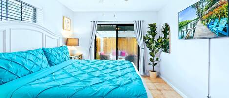 Un dormitorio con cama, ventilador de techo, televisor y vistas al exterior.