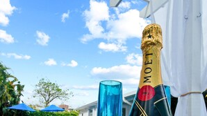 Une bouteille de champagne Moët & Chandon et un verre bleu sur une table en bois, près d’une piscine.