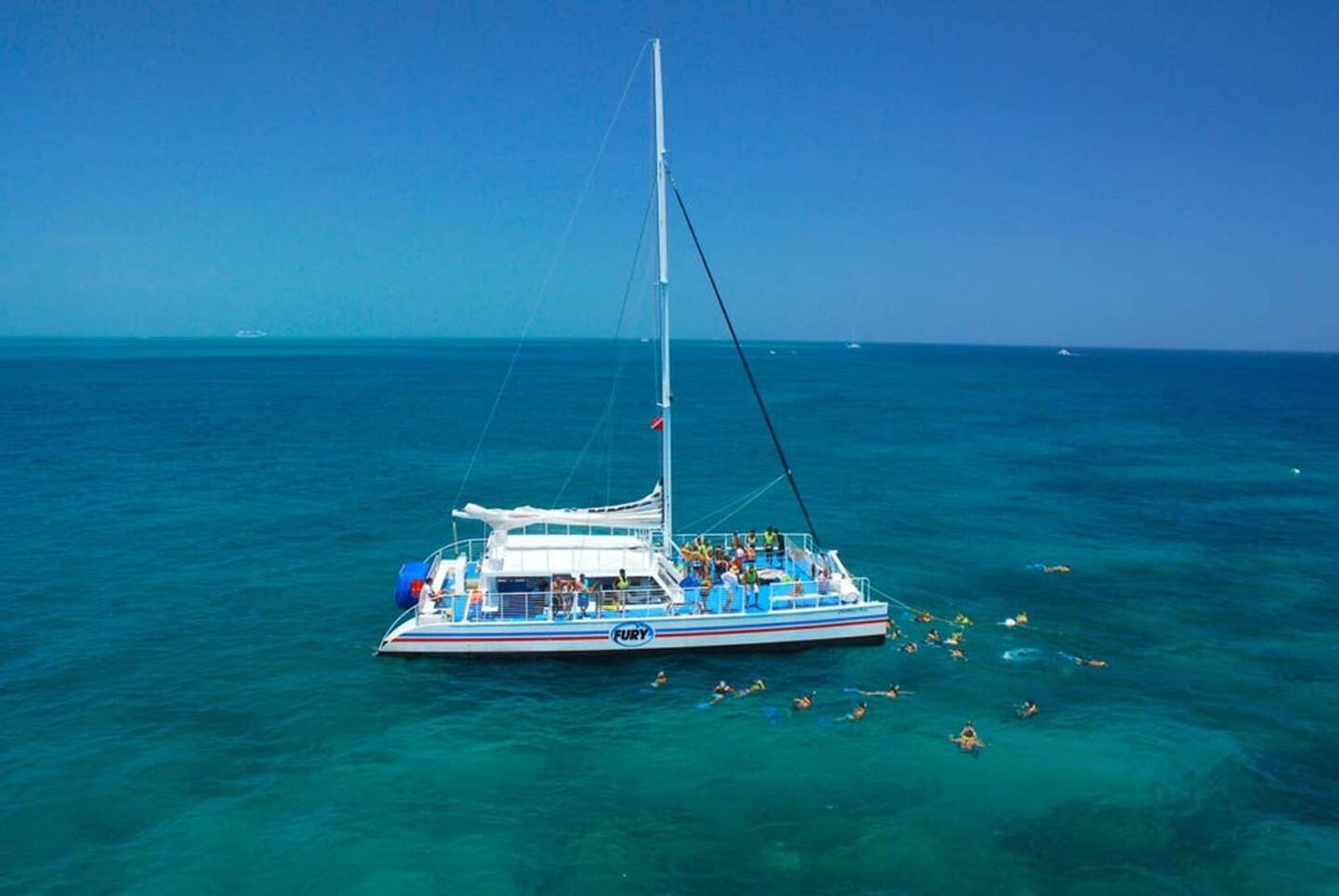 A sailboat with a white hull and blue accents, named 'FURY', floating on turquoise waters with a clear sky above.