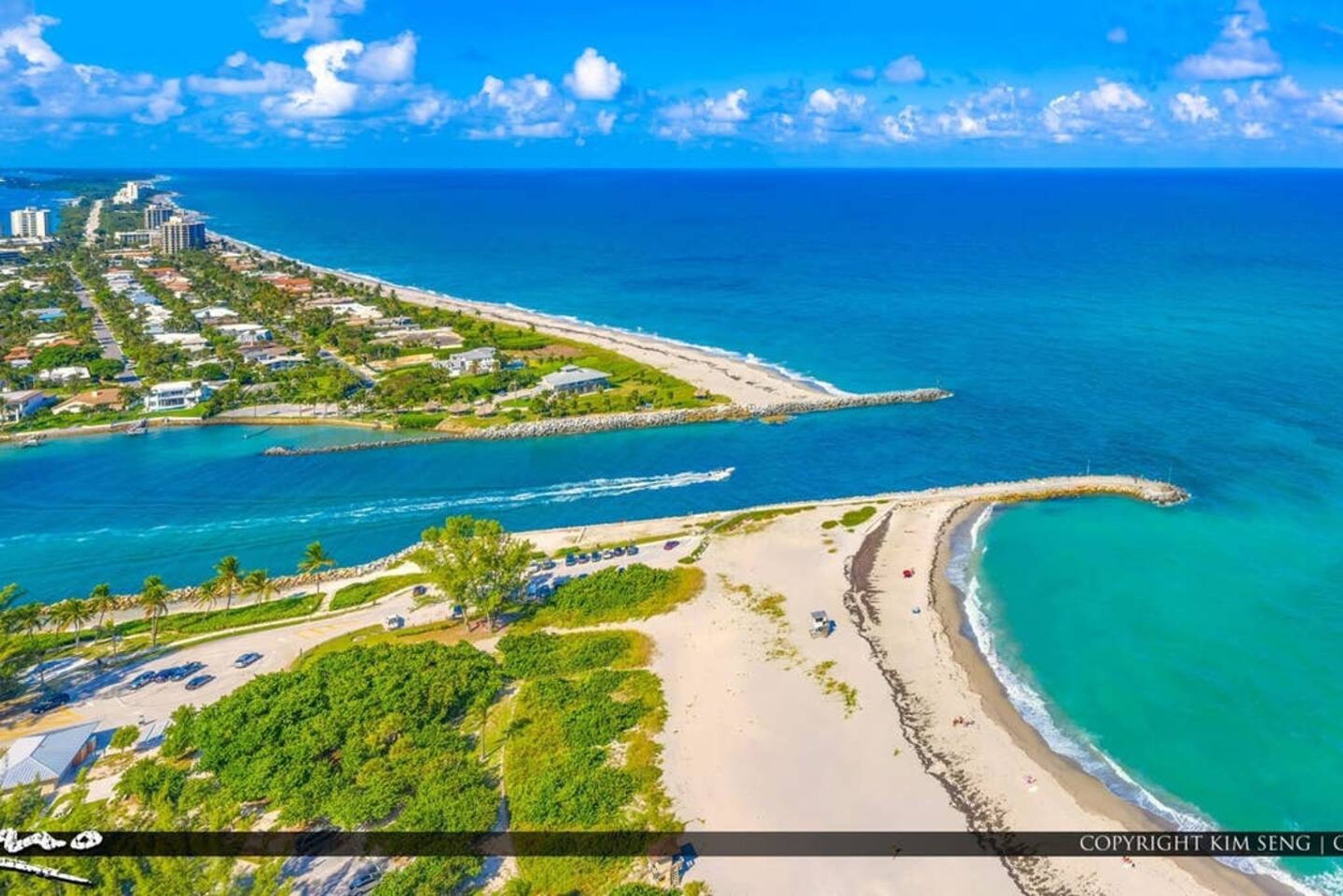 An aerial view of a coastal area with a beach, a marina, and buildings along the shore.