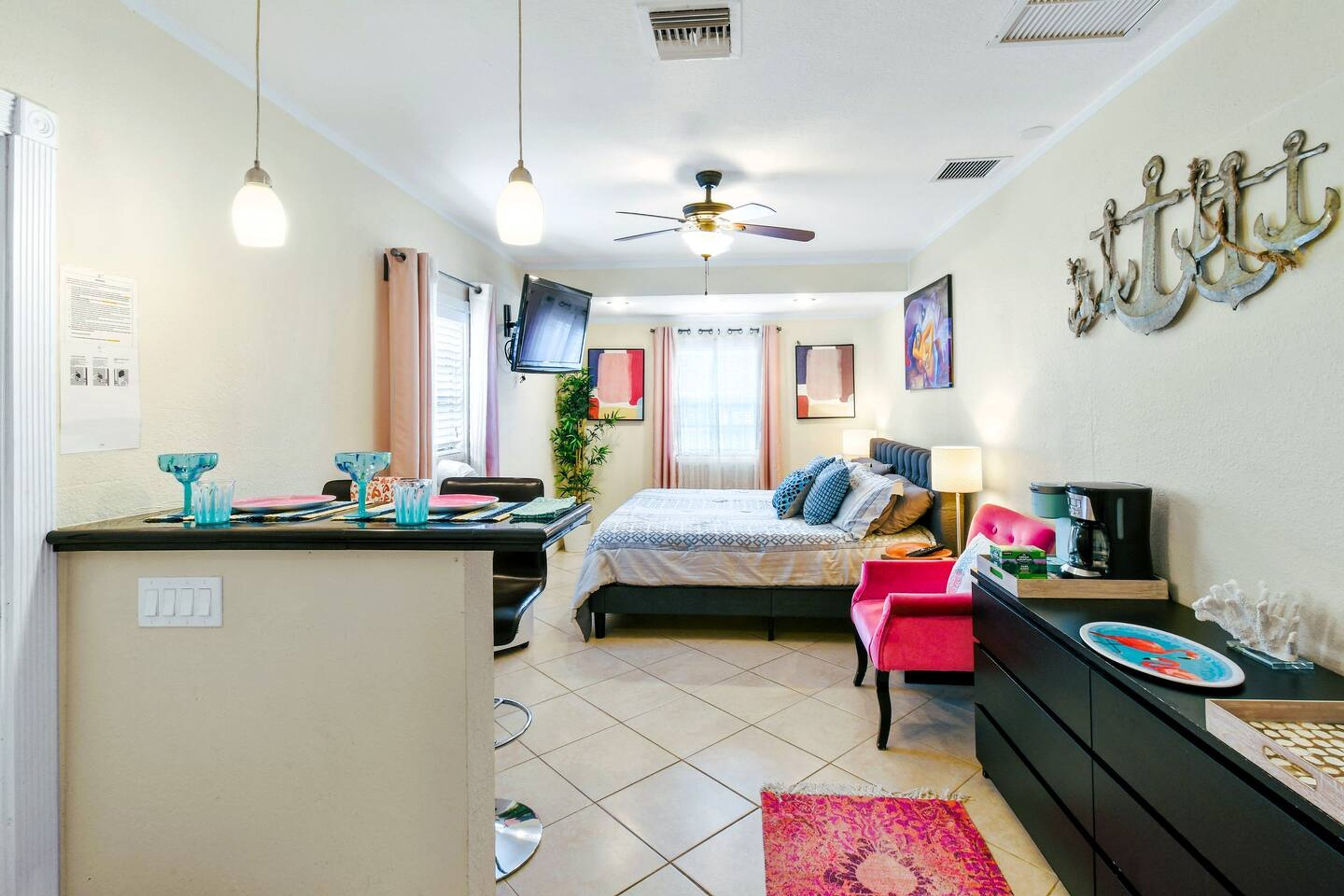 A bedroom with a bed, a desk, a chair, a TV, and a ceiling fan.