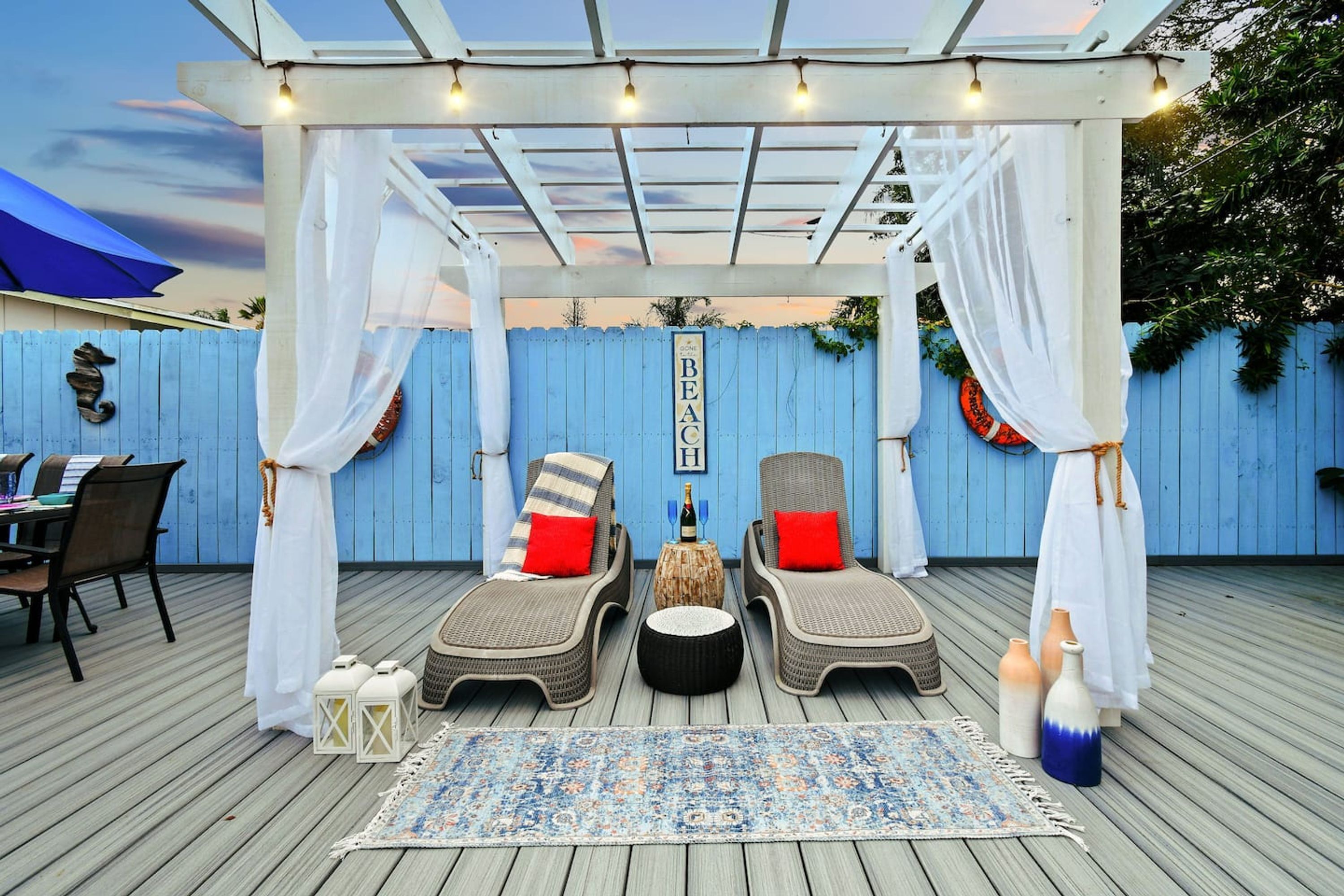 Une terrasse extérieure avec deux fauteuils de jardin en osier, un tapis à motifs et une table sur laquelle se trouve une bouteille.