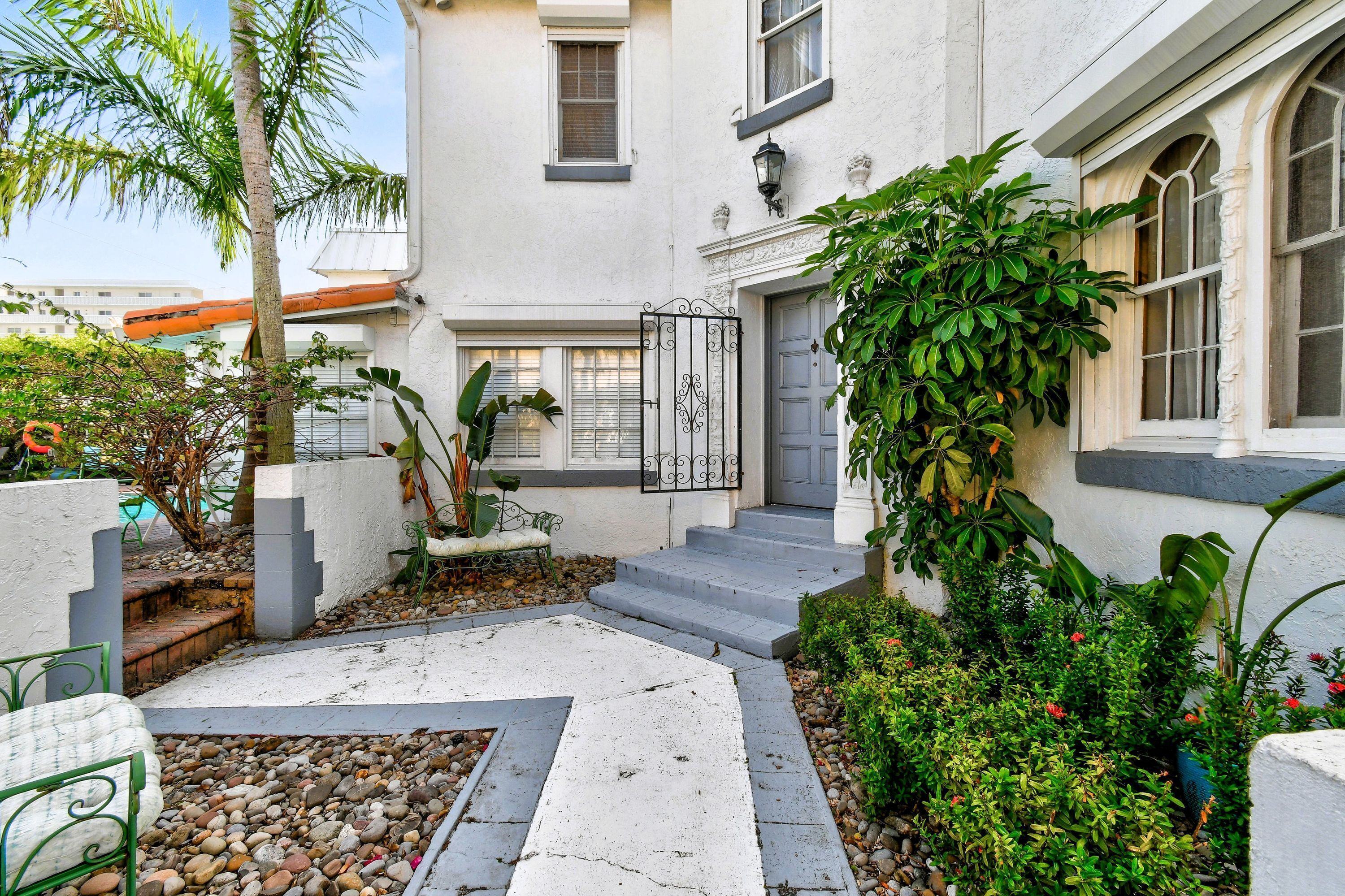 A residential building with a white exterior, a gated entrance, and a small garden area with plants and a pathway.
